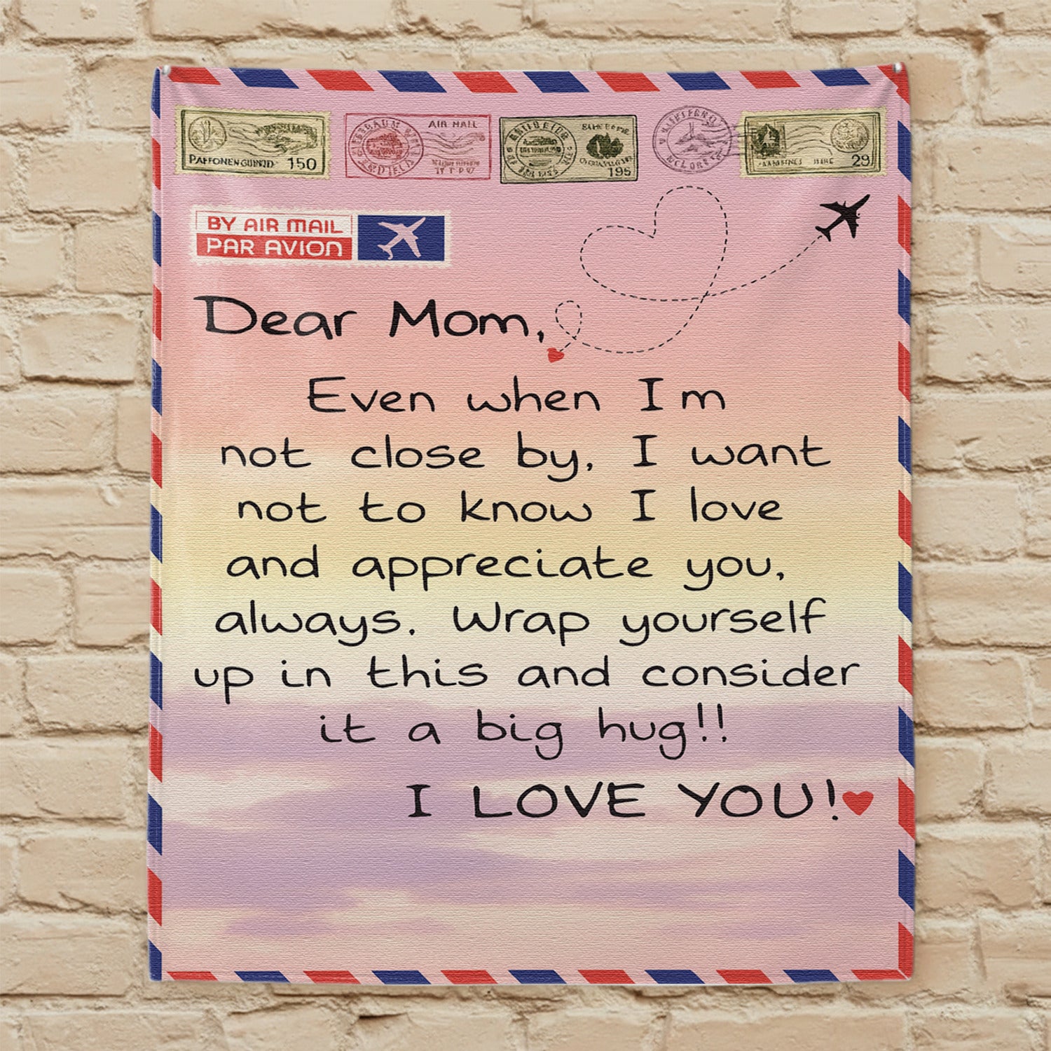 Airmail-style mom blanket with loving long-distance message displayed on a beige brick wall — Discover heartfelt personal gifts at HerTender.com