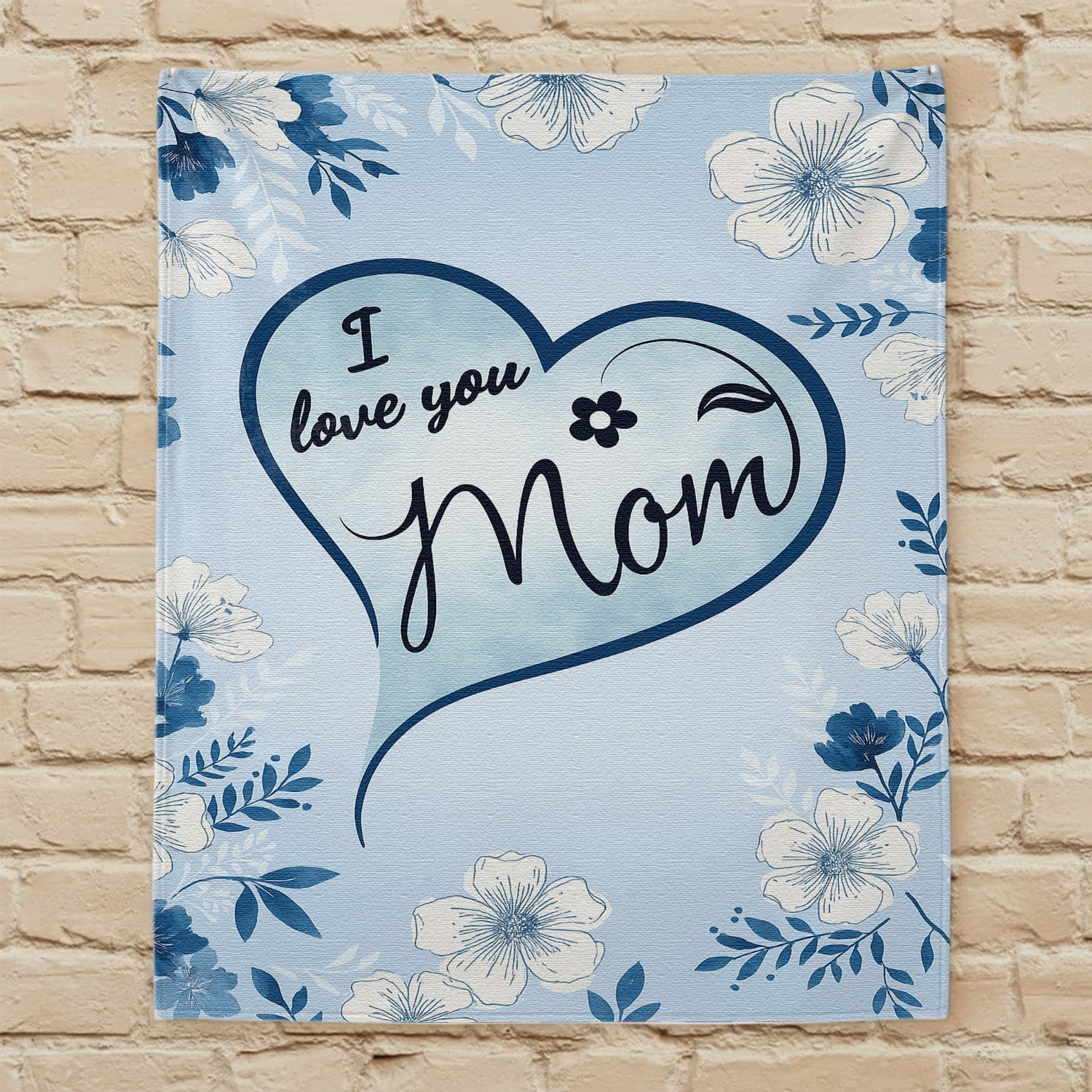 Blue floral mom blanket with heart design and loving message displayed on a beige brick wall — Discover heartfelt personal gifts at HerTender.com