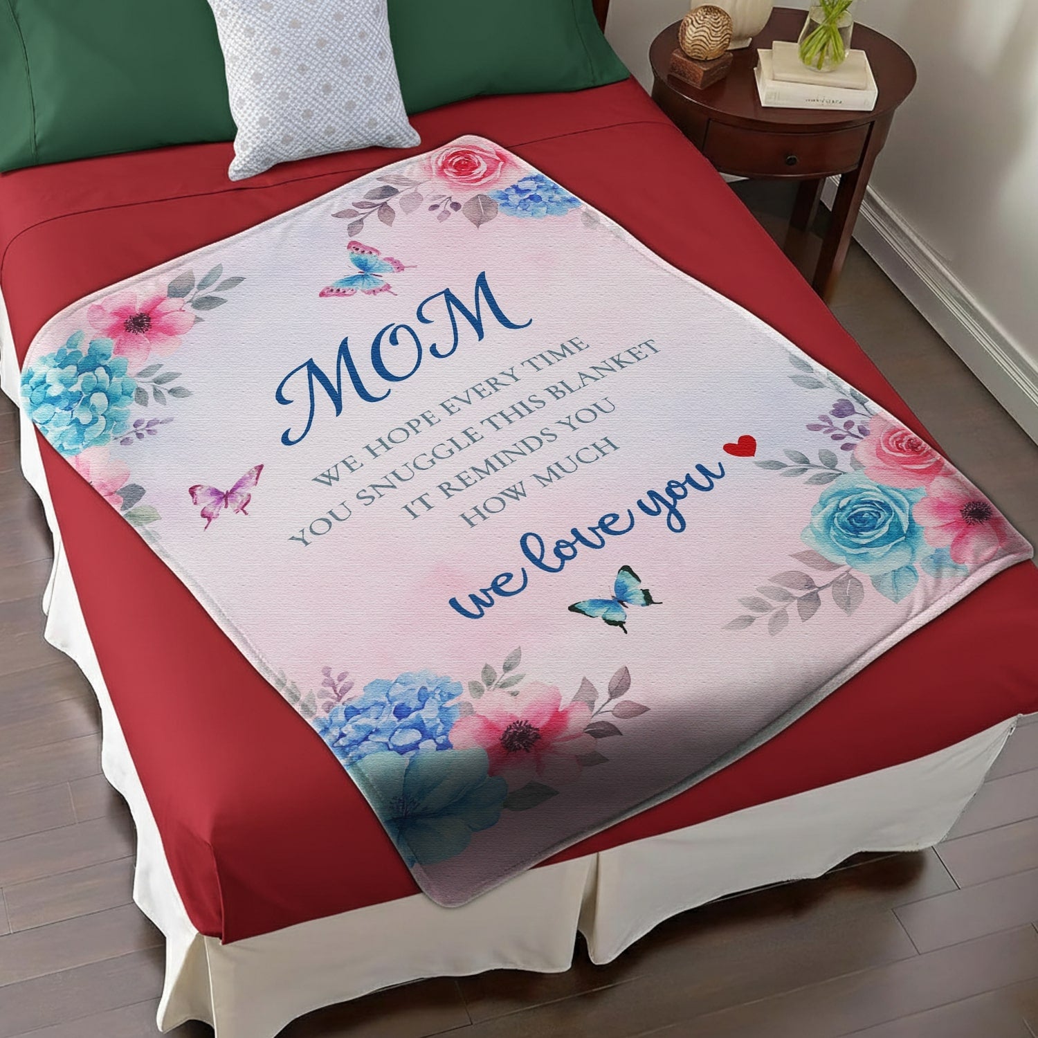 Pastel floral mom blanket with butterflies and loving message displayed on a red and white bed — Discover heartfelt personal gifts at HerTender.com