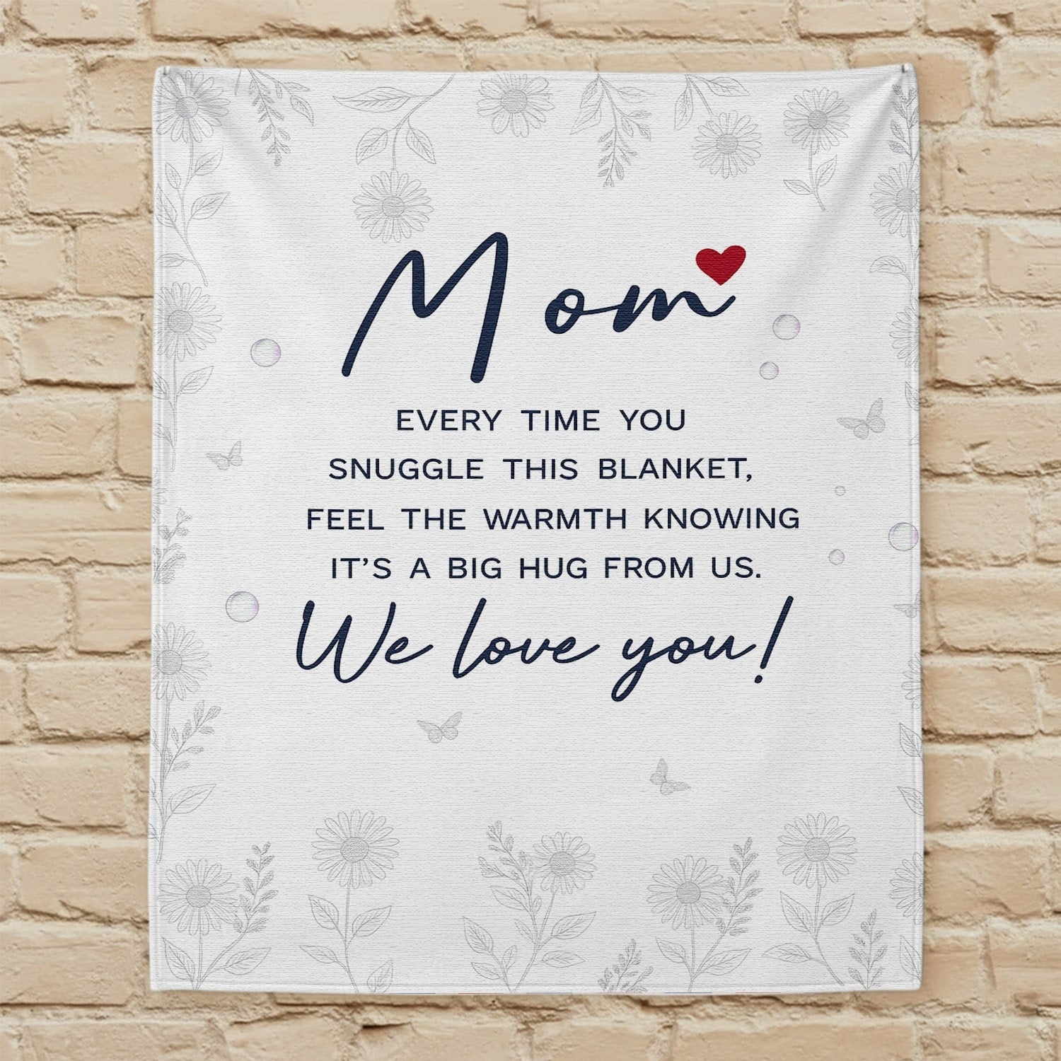 White floral mom blanket with heartfelt message displayed on a beige brick wall — Discover heartfelt personal gifts at HerTender.com