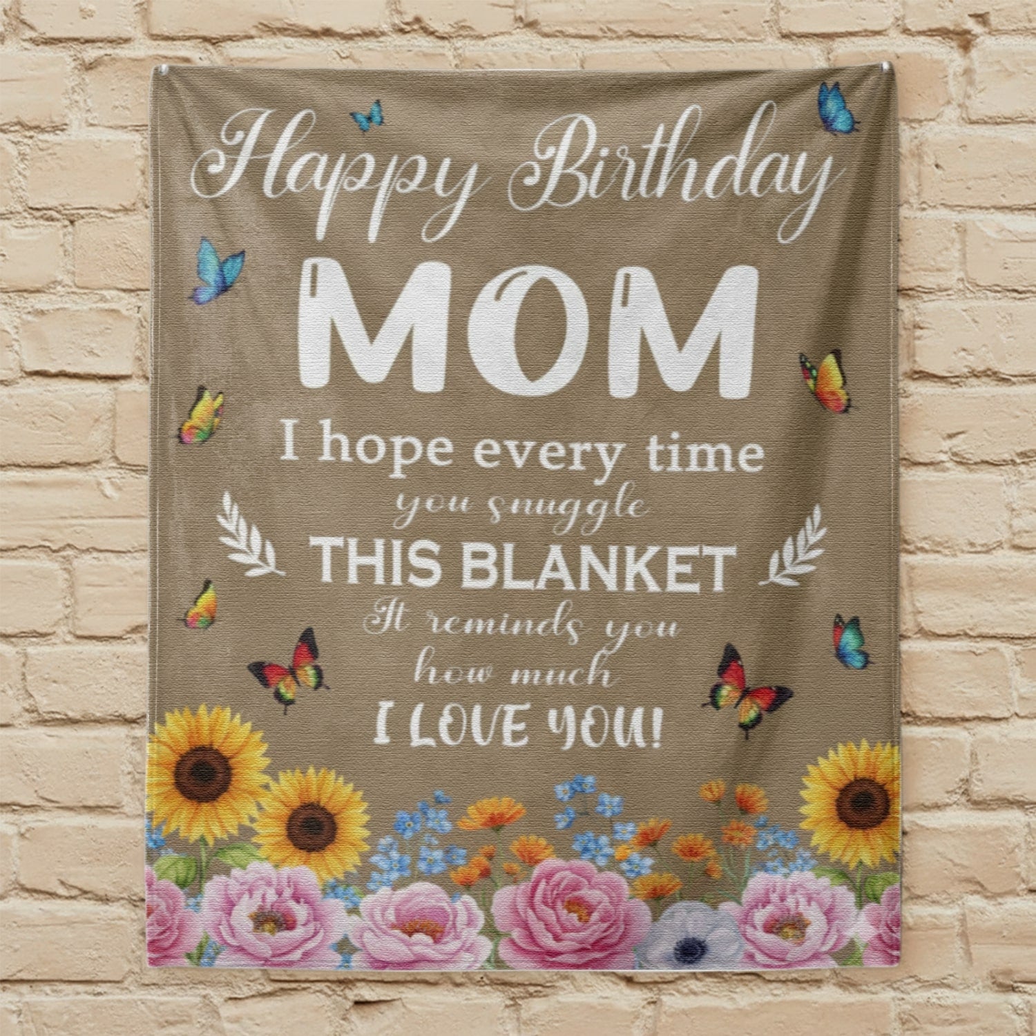 Happy Birthday Mom blanket with butterflies and flowers hanging on a beige brick wall, symbolizing personalized gifts — Discover heartfelt personalized gifts at HerTender.com.