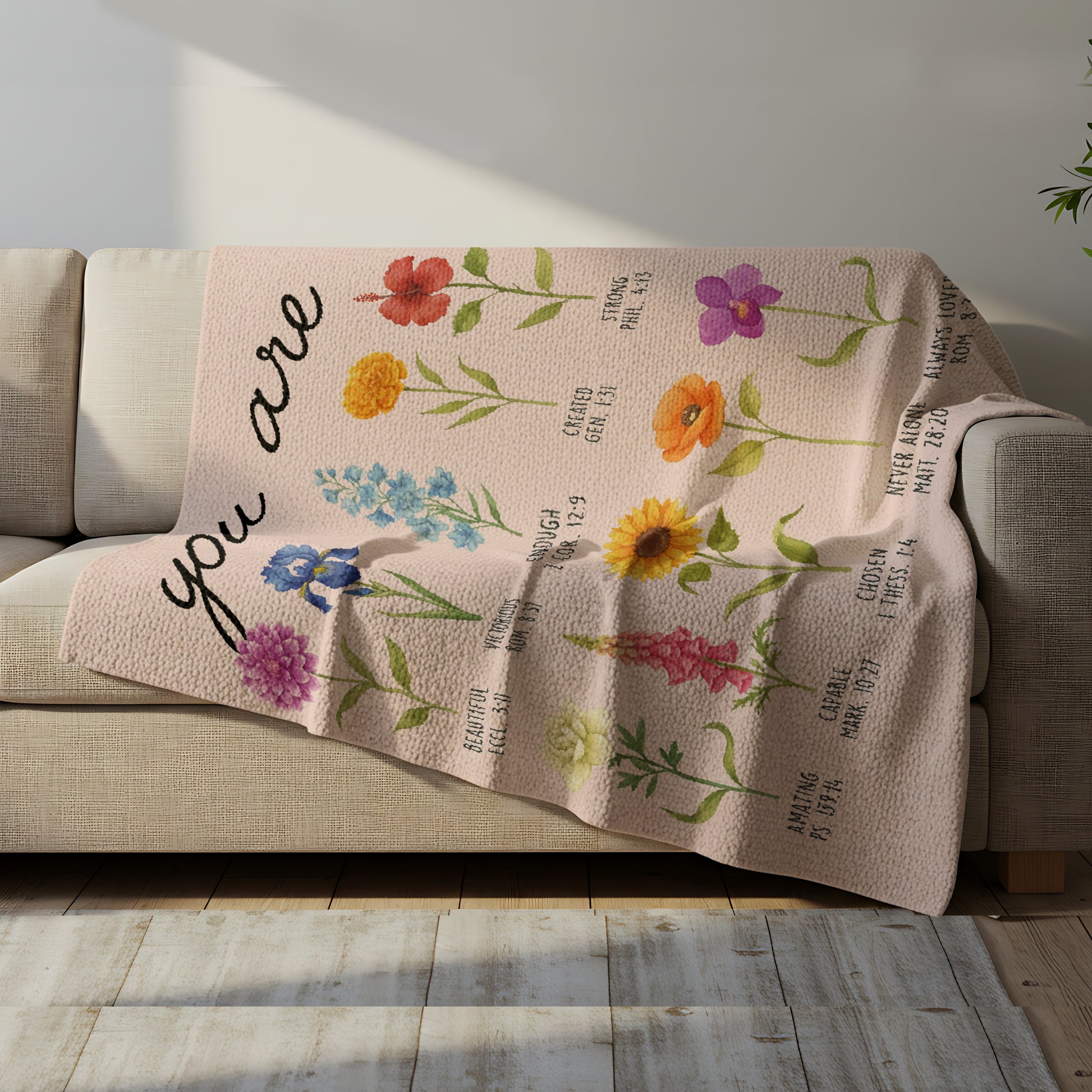Floral blanket with the words “You Are” and Bible verse affirmations draped over a cozy sofa, symbolizing faith-inspired personalized gifts — Discover heartfelt personalized gifts at HerTender.com.