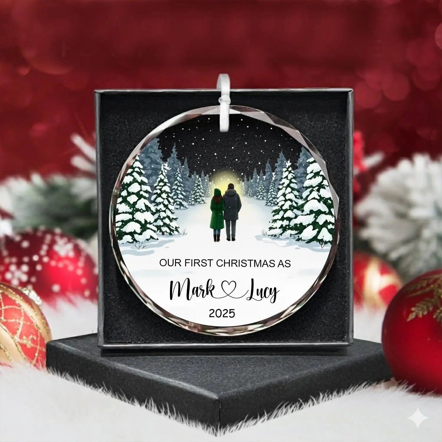 Round personalized glass ornament with snowy forest couple design and text “Our First Christmas As Mark and Lucy 2025,” beautifully packaged in a gift box — a timeless keepsake for newlyweds, available at Hertender.com.