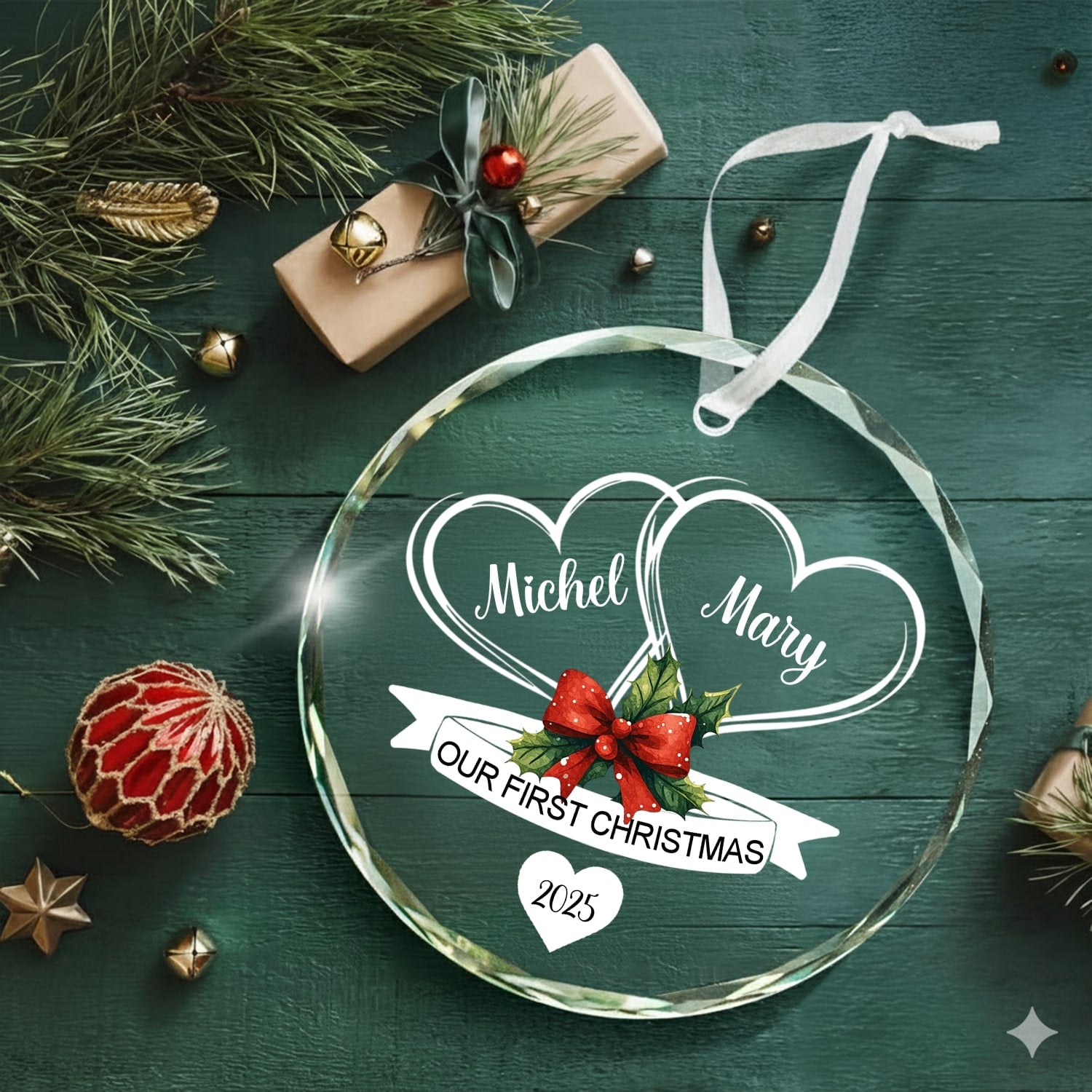 Round glass ornament engraved with two hearts and red bow reading “Our First Christmas 2025” on a rustic green background — Discover romantic personalized Christmas gifts at Hertender.com.