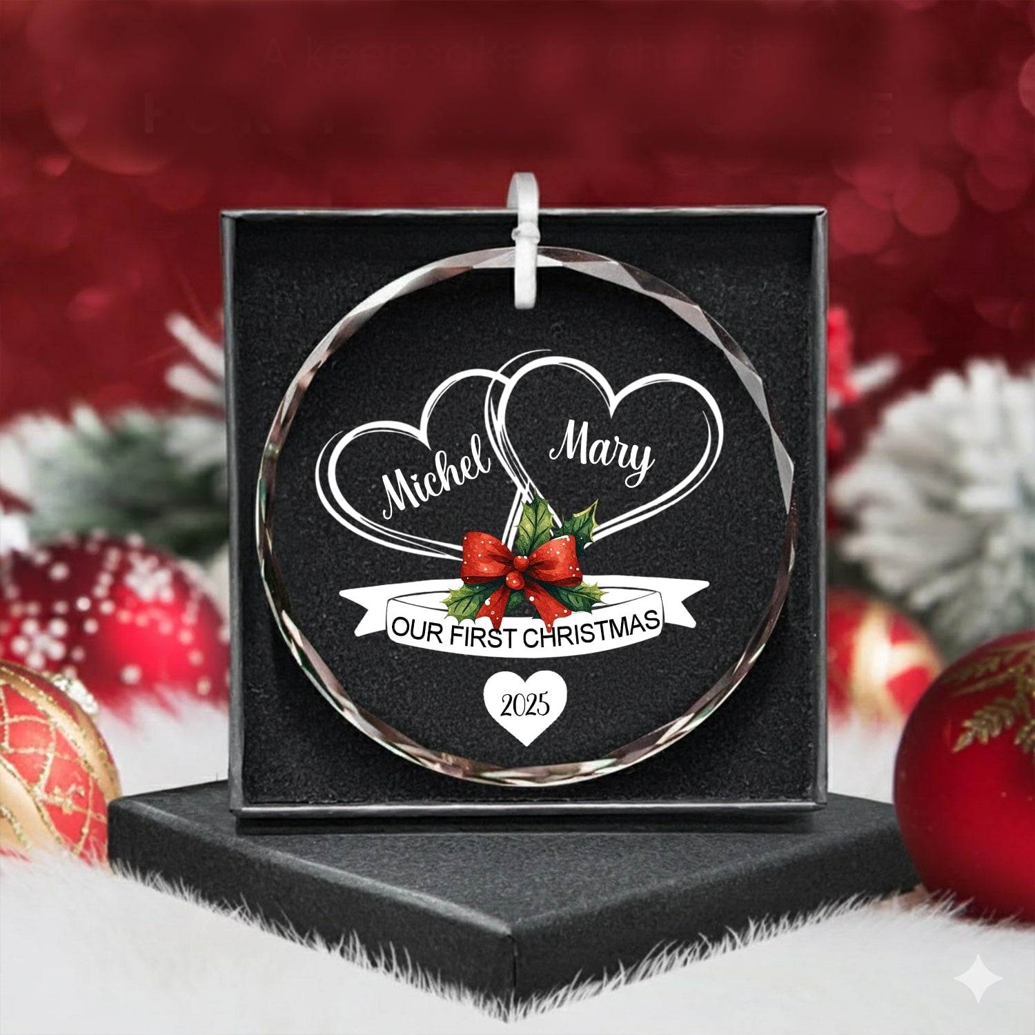 Round glass ornament engraved with two hearts and red bow reading “Our First Christmas 2025” in a black gift box with festive decor — Discover romantic personalized Christmas gifts at Hertender.com.