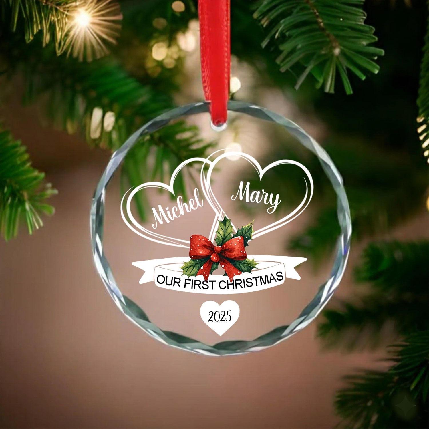 Round glass ornament with red ribbon engraved with two hearts and red bow reading “Our First Christmas 2025” on a Christmas tree — Celebrate love with heartfelt personalized Christmas gifts at Hertender.com.