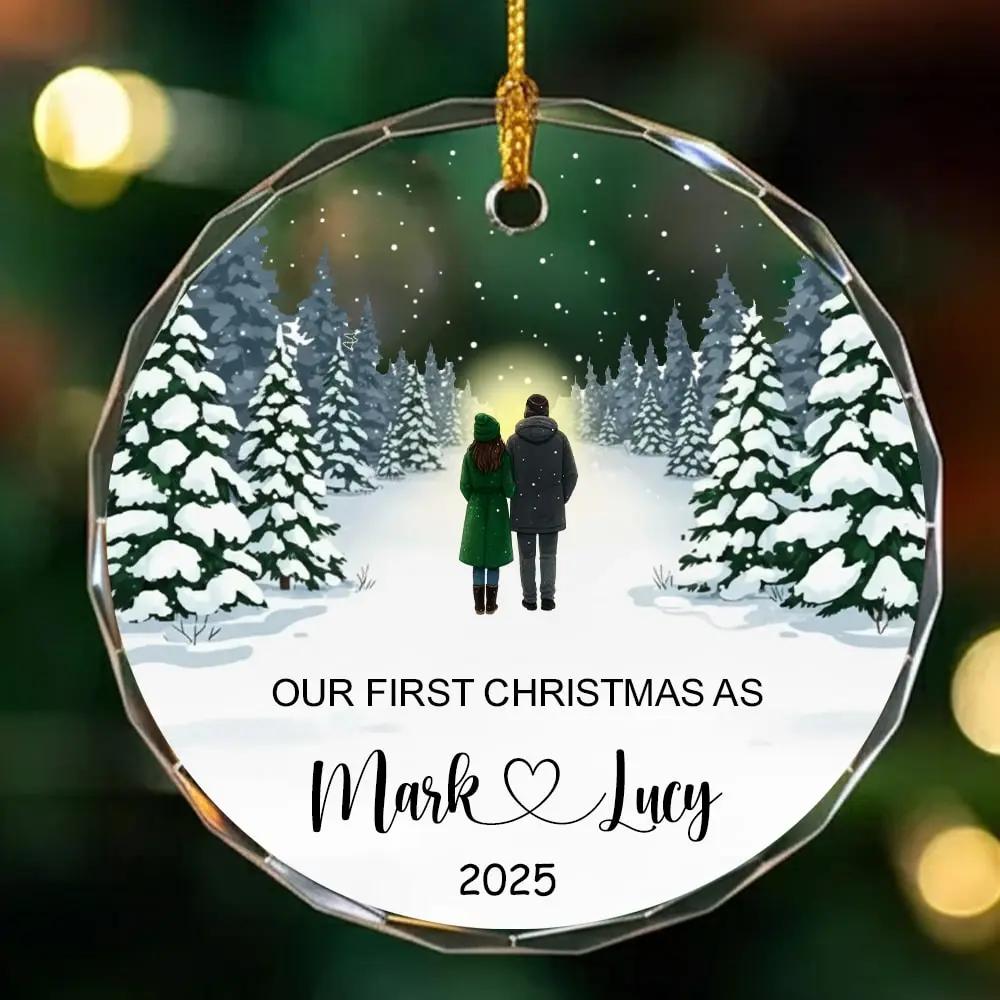 Round personalized glass ornament with a winter forest couple design and text “Our First Christmas As Mark and Lucy 2025” — Celebrate your love story with romantic personalized gifts from Hertender.com.